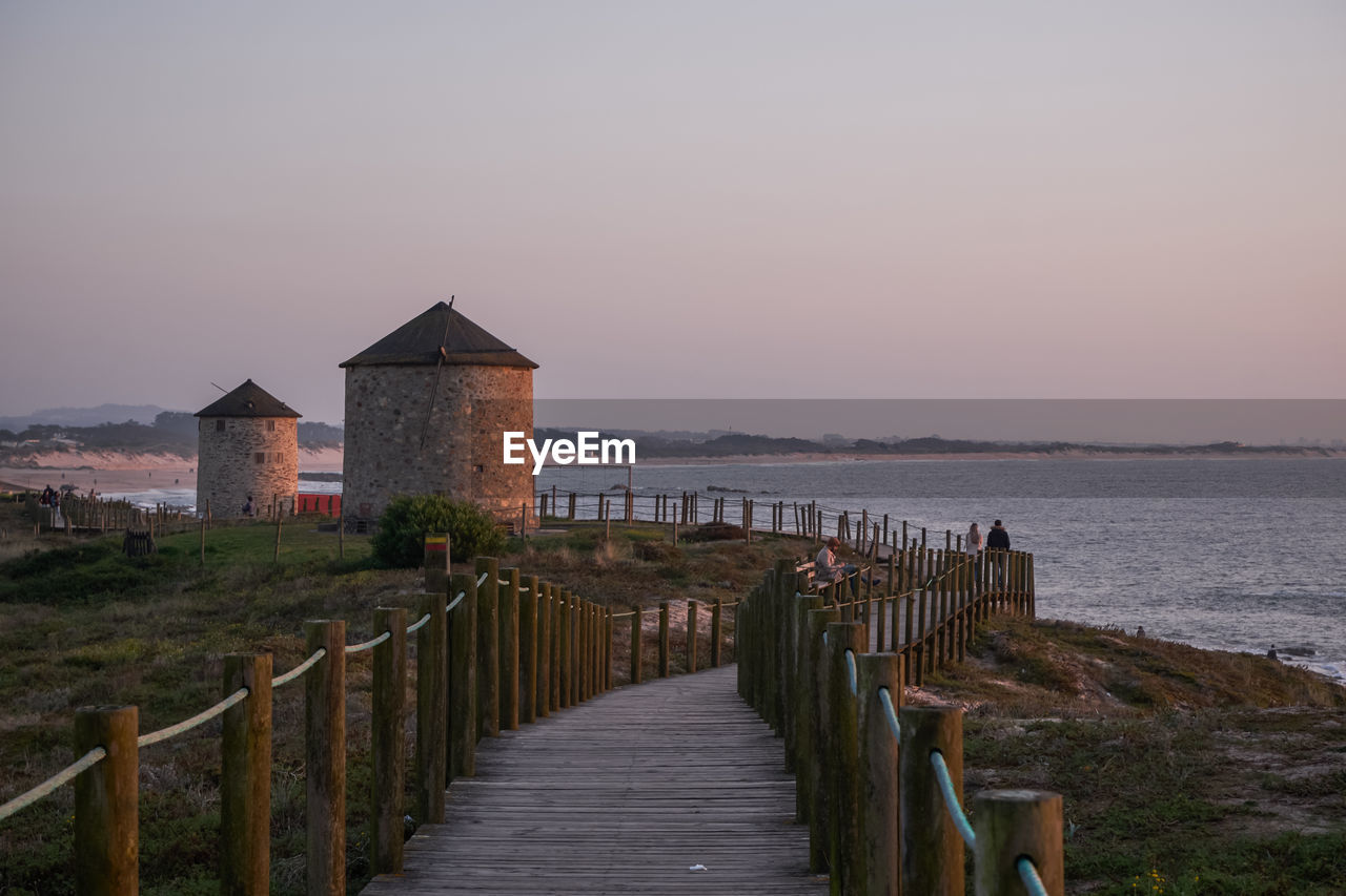WOODEN POSTS BY SEA AGAINST BUILDINGS AGAINST CLEAR SKY