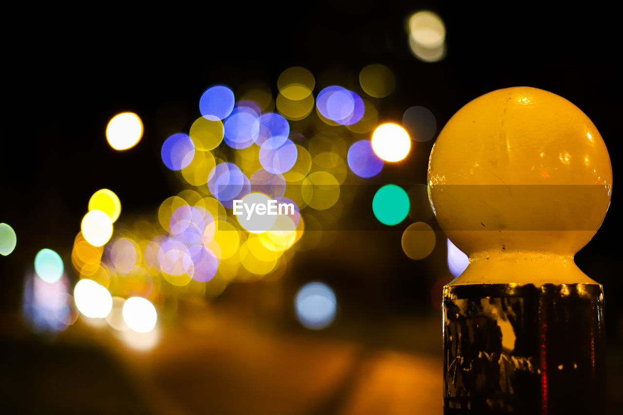 Close-up of bollard against lights in city at night