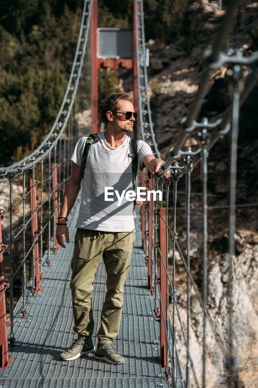 Portrait of middle-aged hiker passing by the hanging bridge and looking away. travel concept