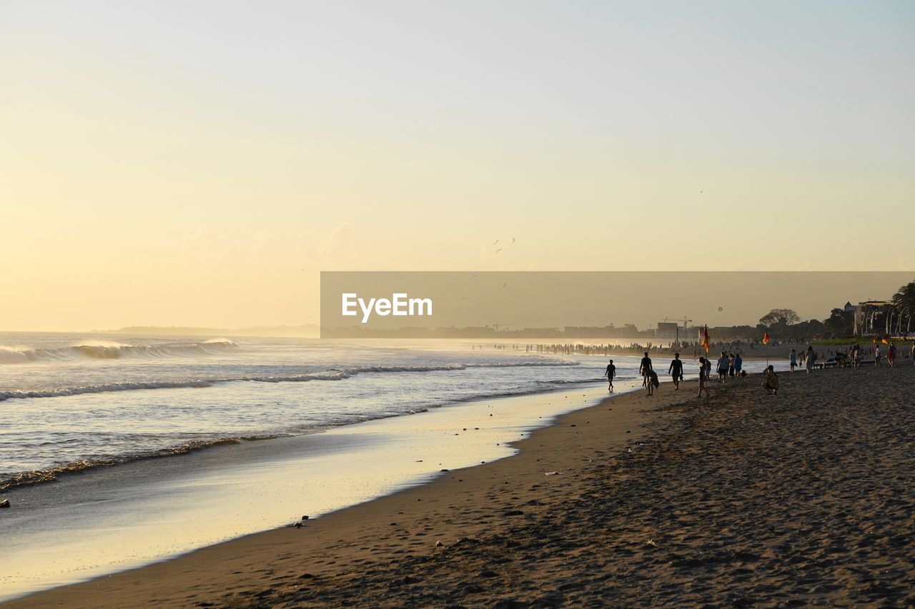 People on beach against clear sky during sunset