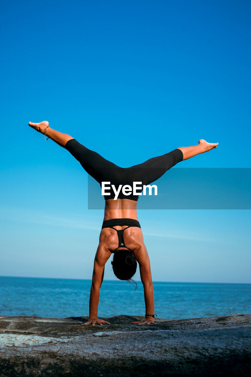 Full length of mature woman practicing handstand by sea against sky