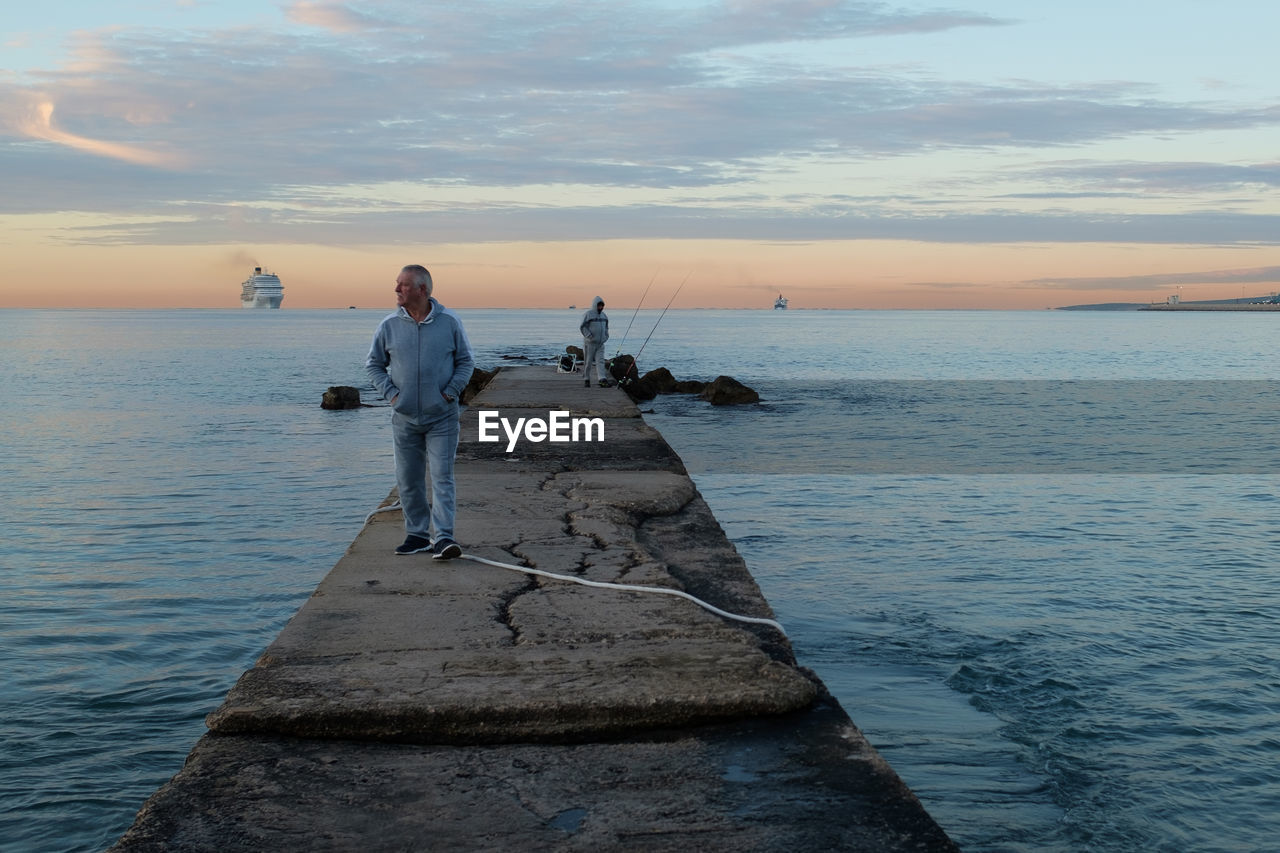 PEOPLE STANDING ON ROCK AT SEA SHORE AGAINST SKY