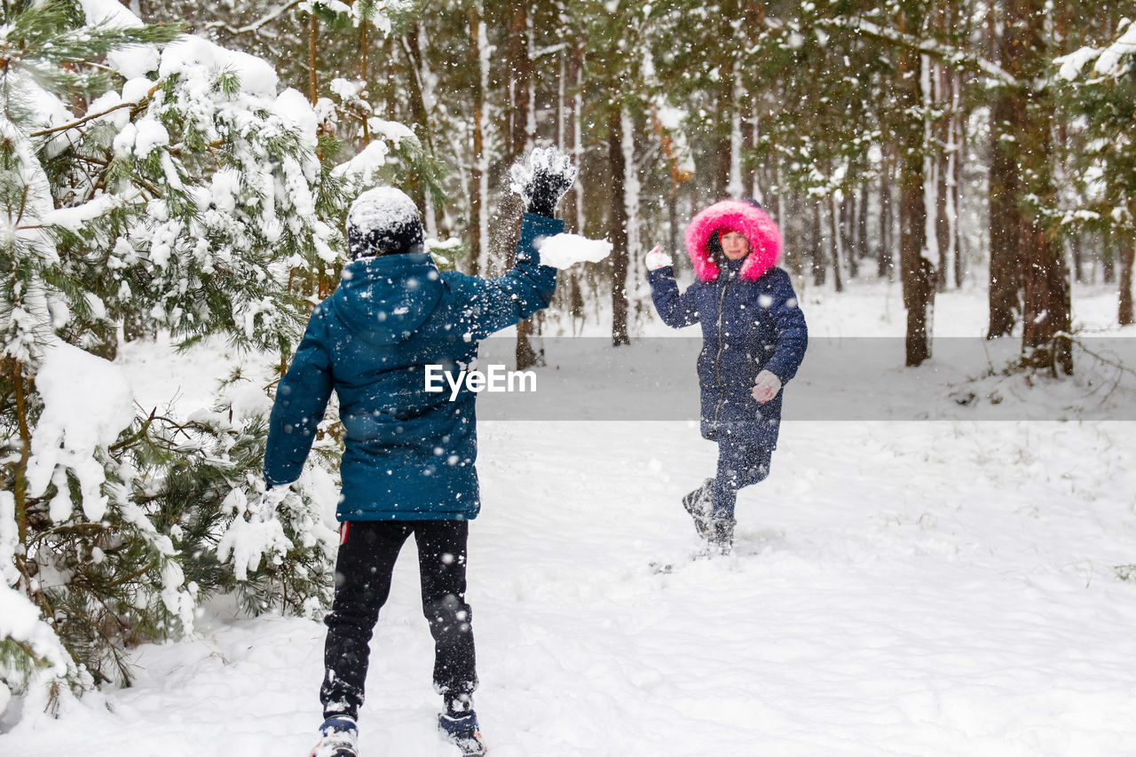 Boy swinging a snowball with a girl. funny children in winter park playing snowballs, actively