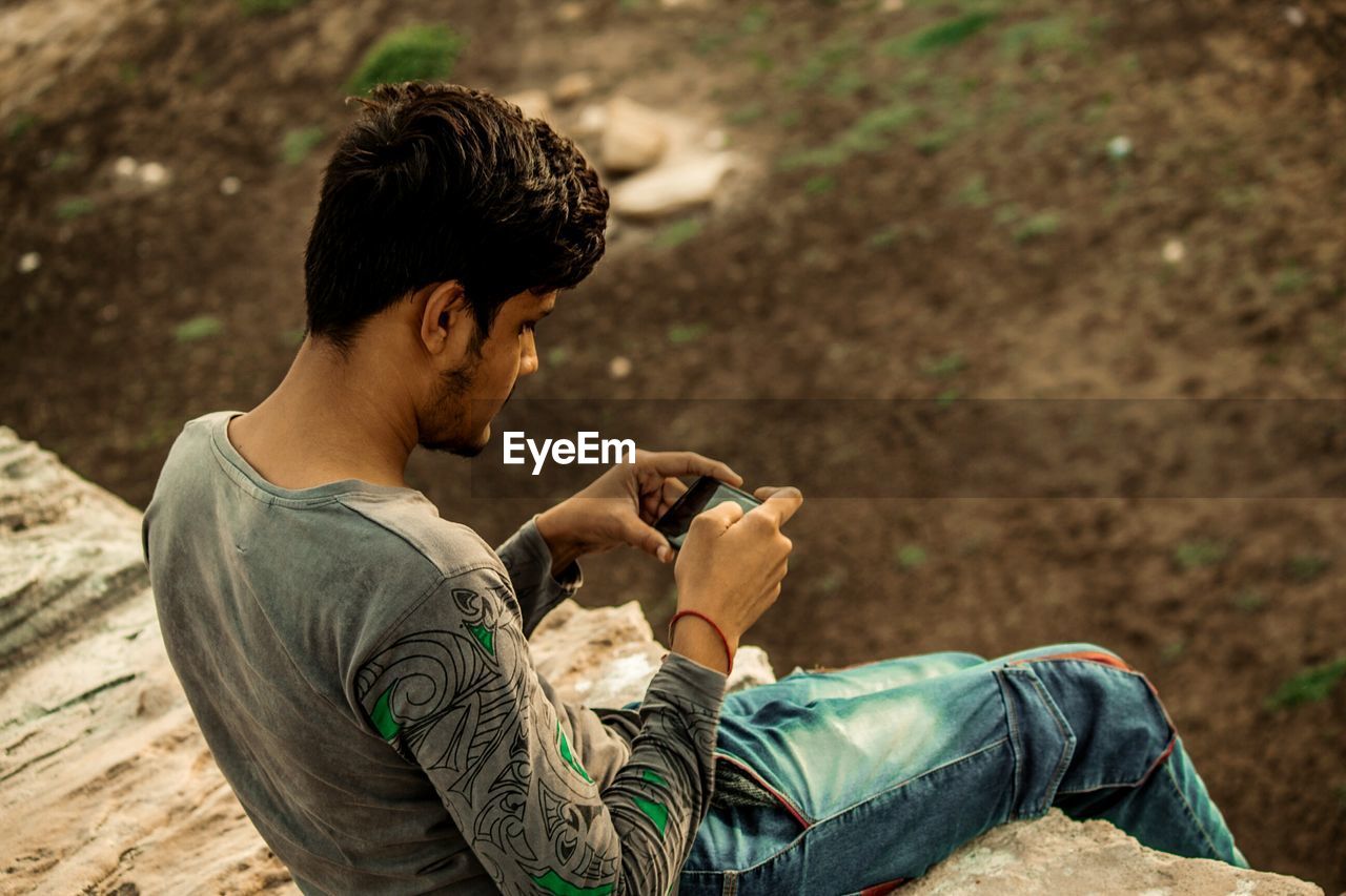 Man photographing while sitting on rock