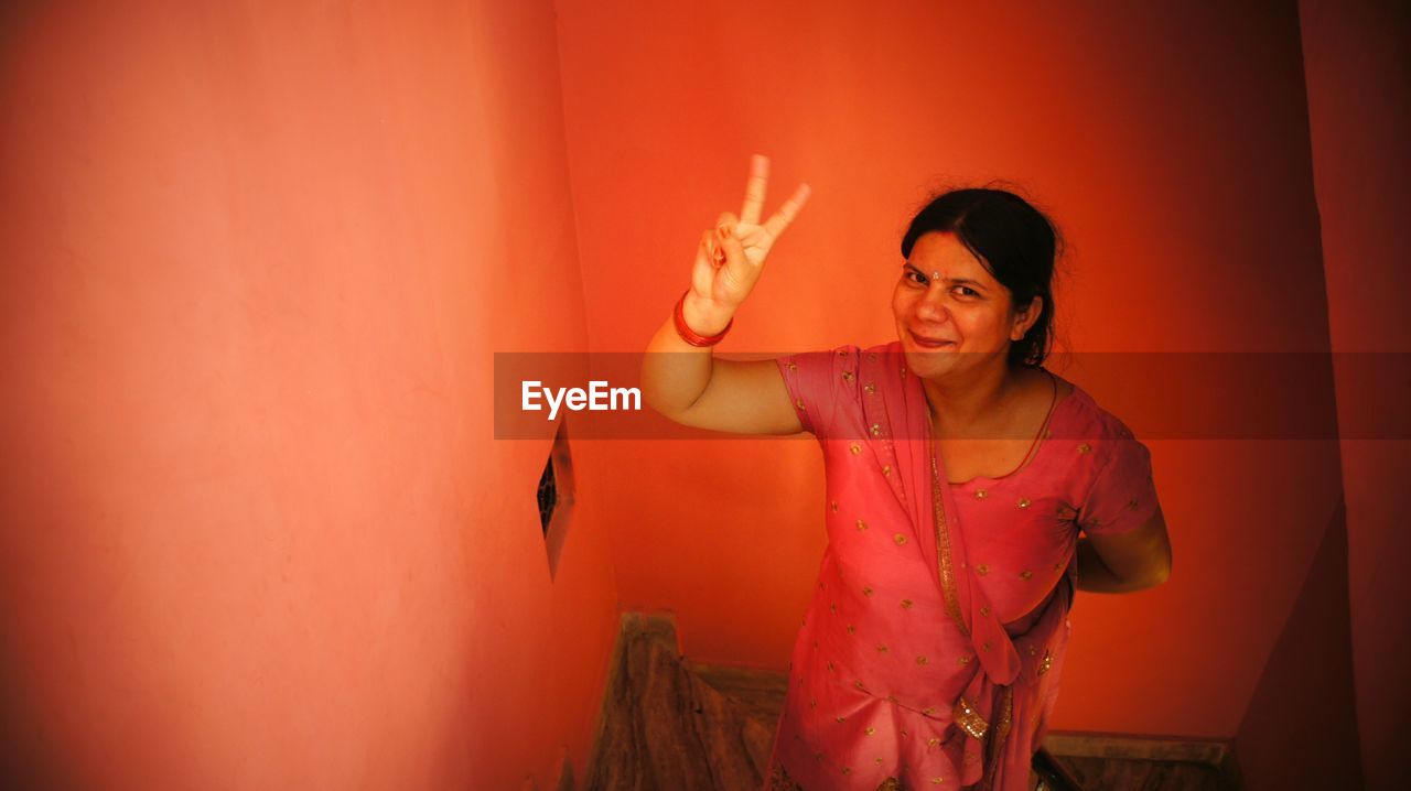 High angle portrait of smiling woman gesturing peace sign at home