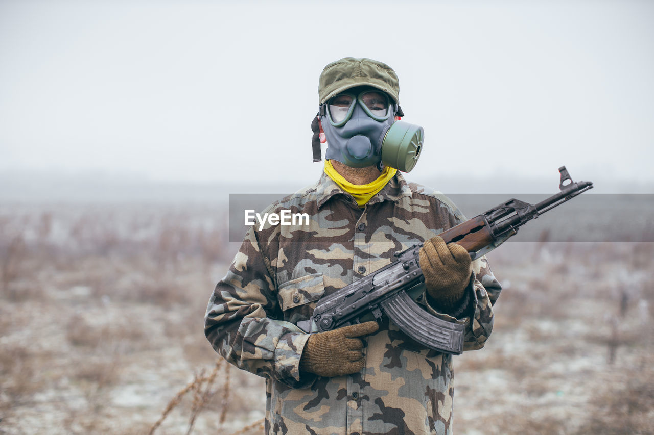 Portrait of soldier holding rifle standing against snow covered land during winter