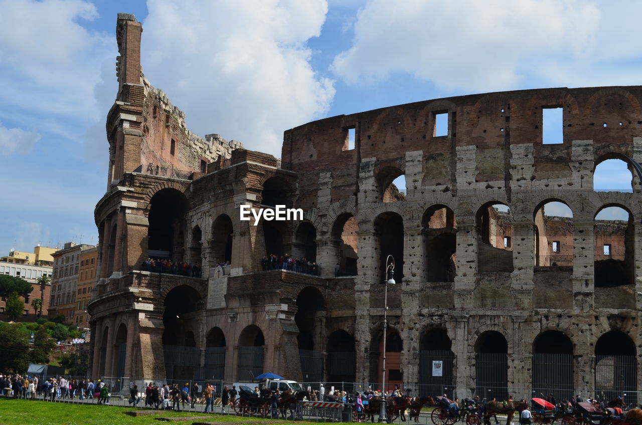 People visiting coliseum against cloudy sky