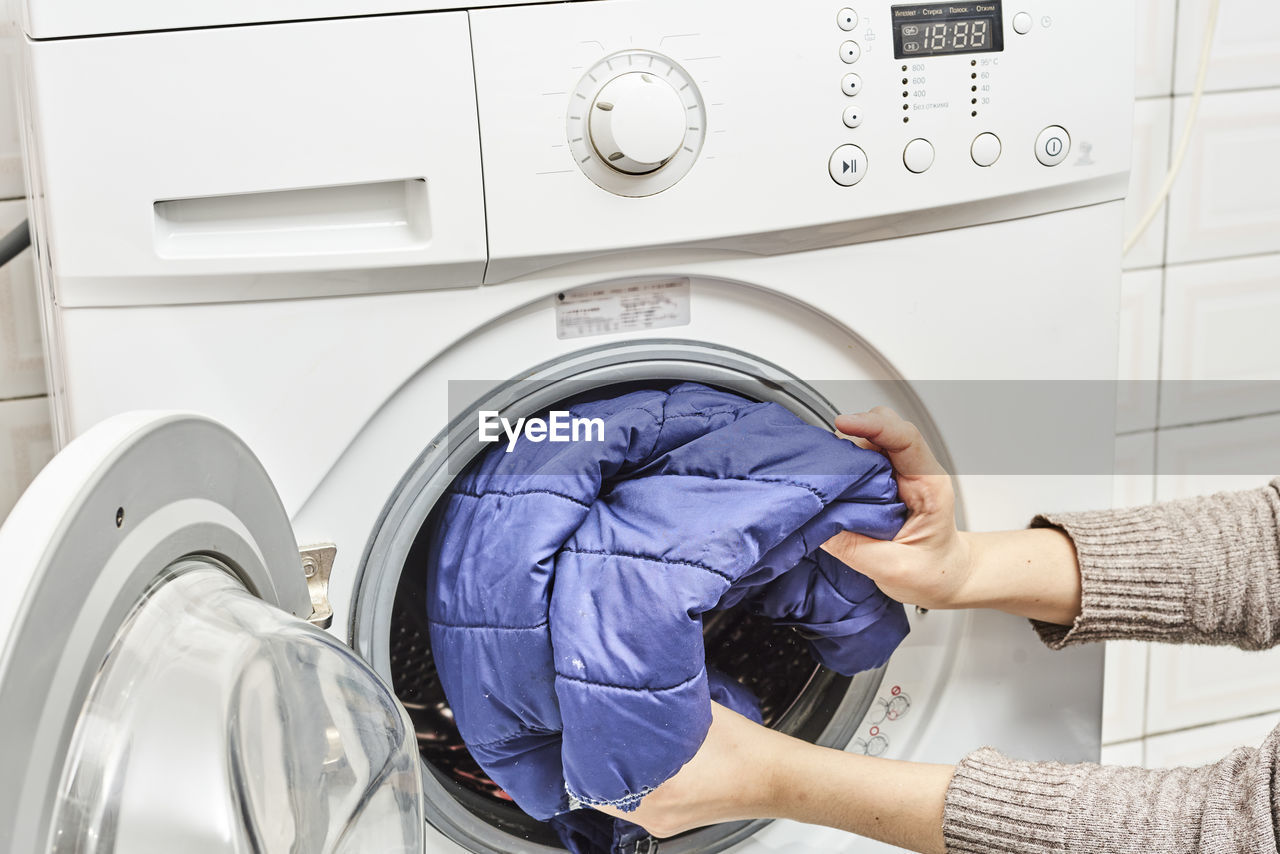 Unrecognizable woman washing dirty laundry in the washing machine