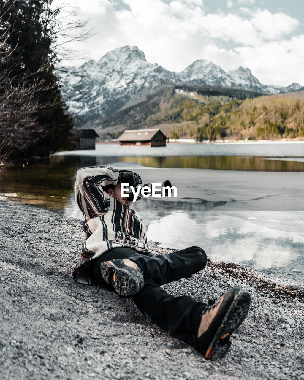 Full length of man photographing while lying down by lake against sky