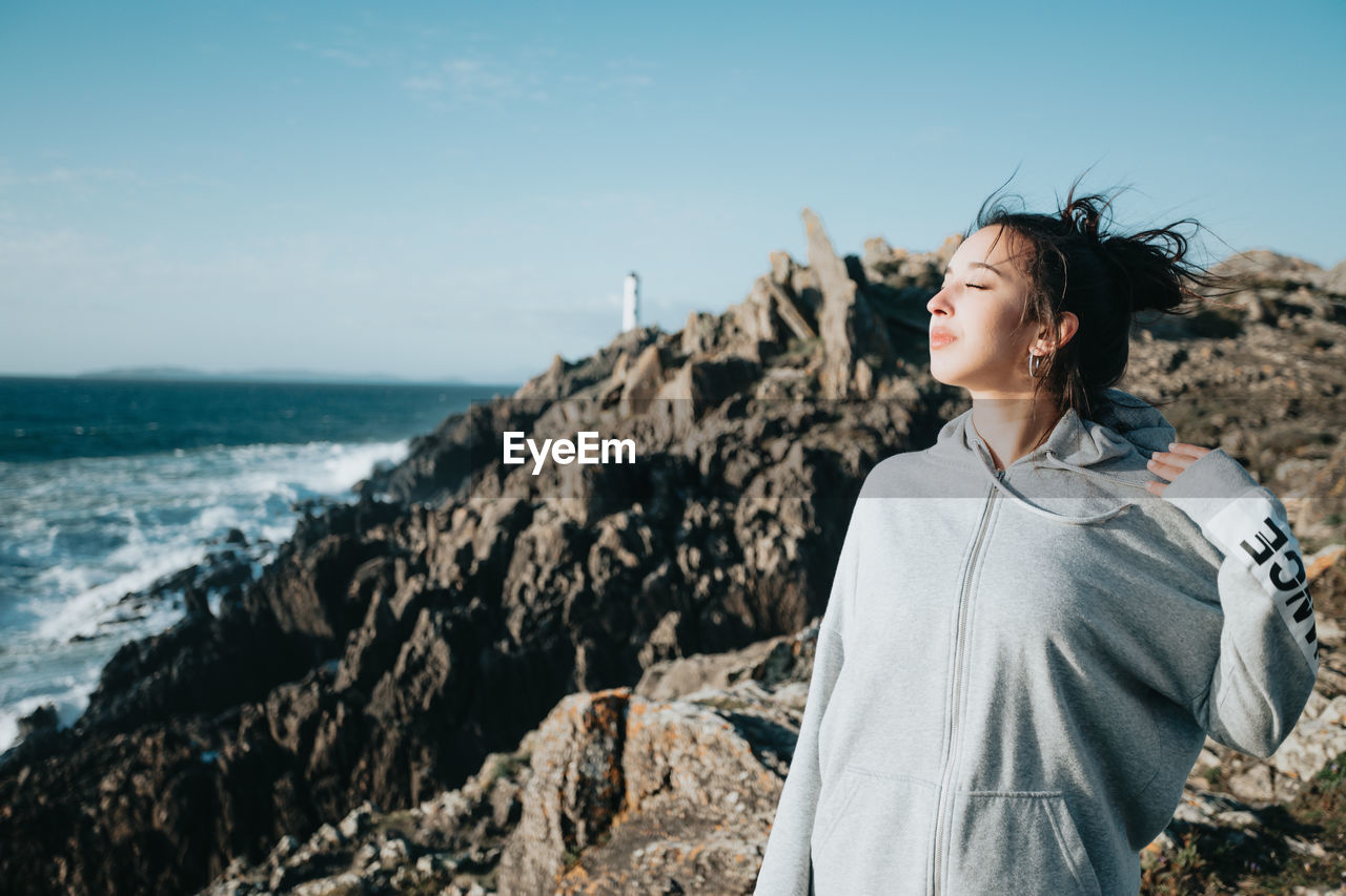 Side view of young woman standing at beach against sky