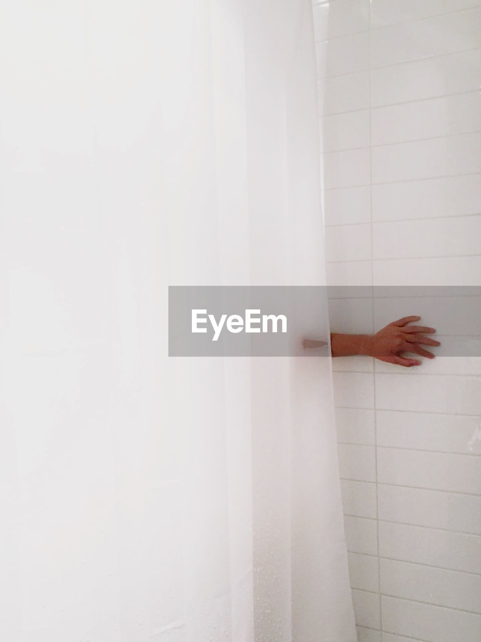 Cropped hand against tiled wall in bathroom