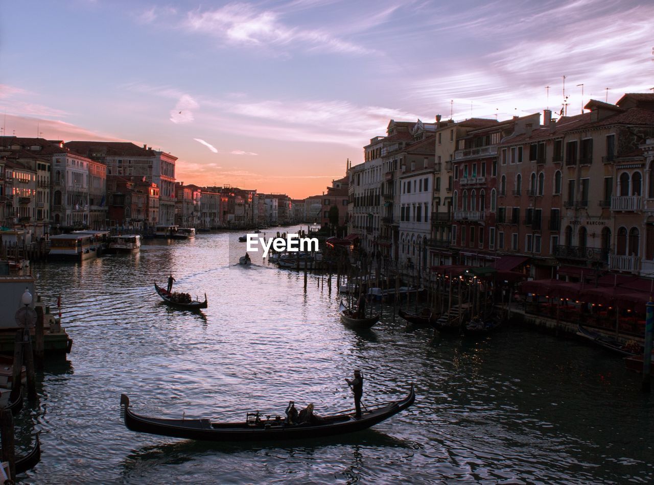 Gondolas on canal in city against sky during sunset