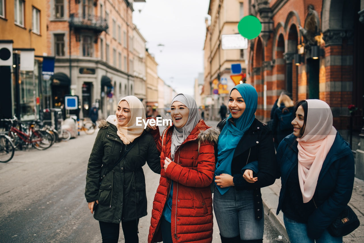 Happy multi-ethnic muslim female friends standing on street in city