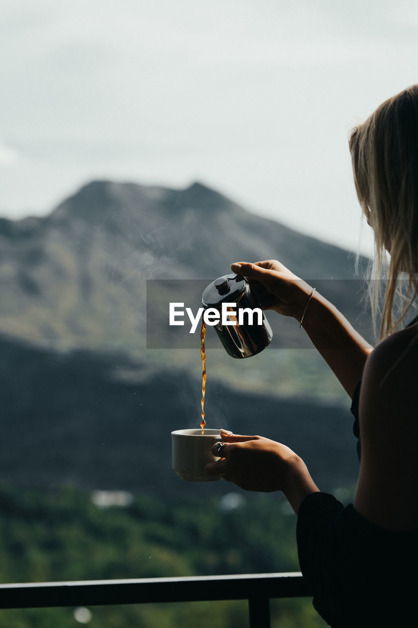 Woman pouring coffee in cup against mountain
