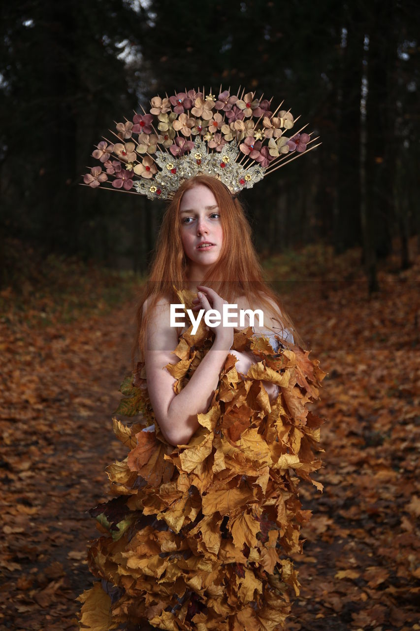 Thoughtful young woman wearing flowers on hair standing at forest during autumn