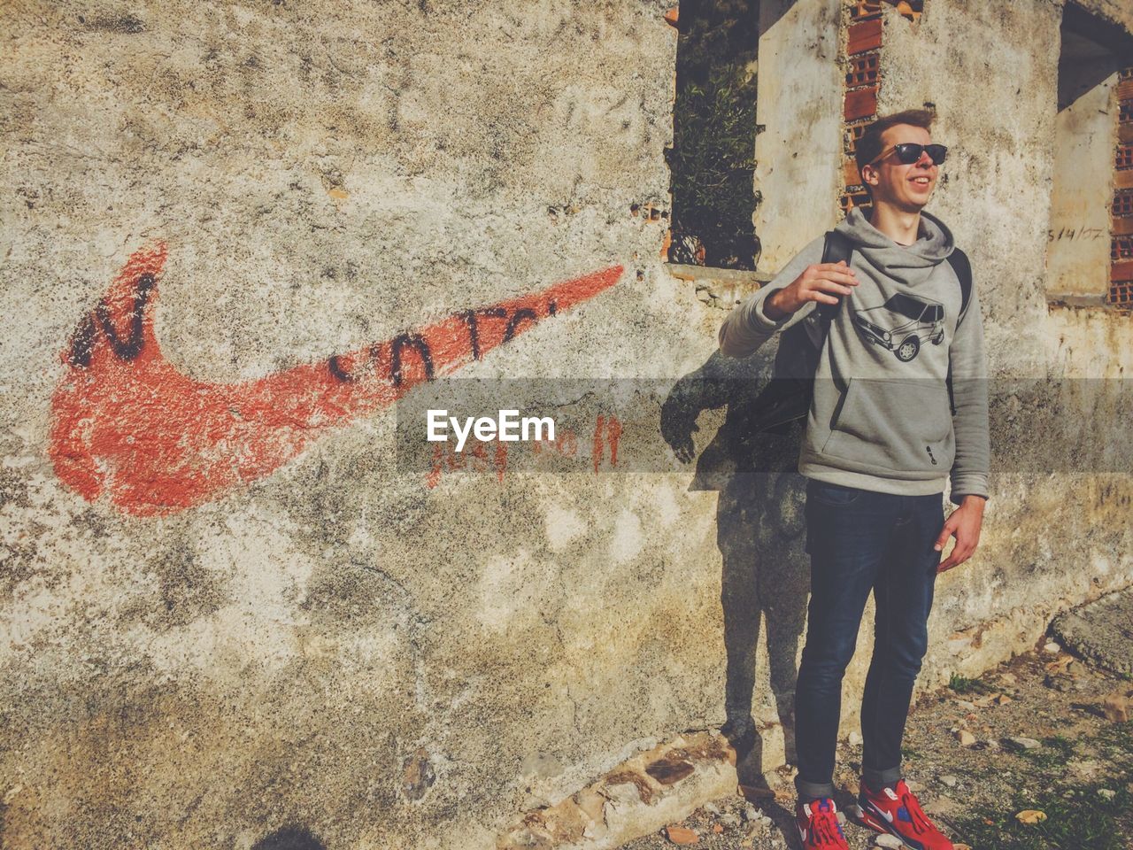 FULL LENGTH OF A YOUNG MAN STANDING BY WALL