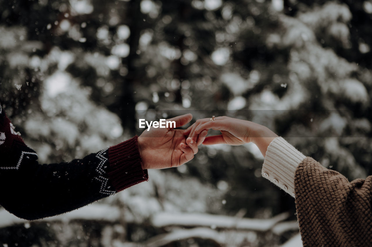 Cropped image of couple holding hands in forest during winter