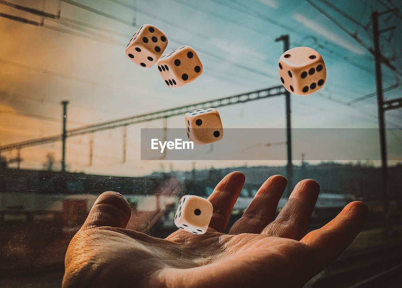 Cropped hand of man throwing dice in air by window