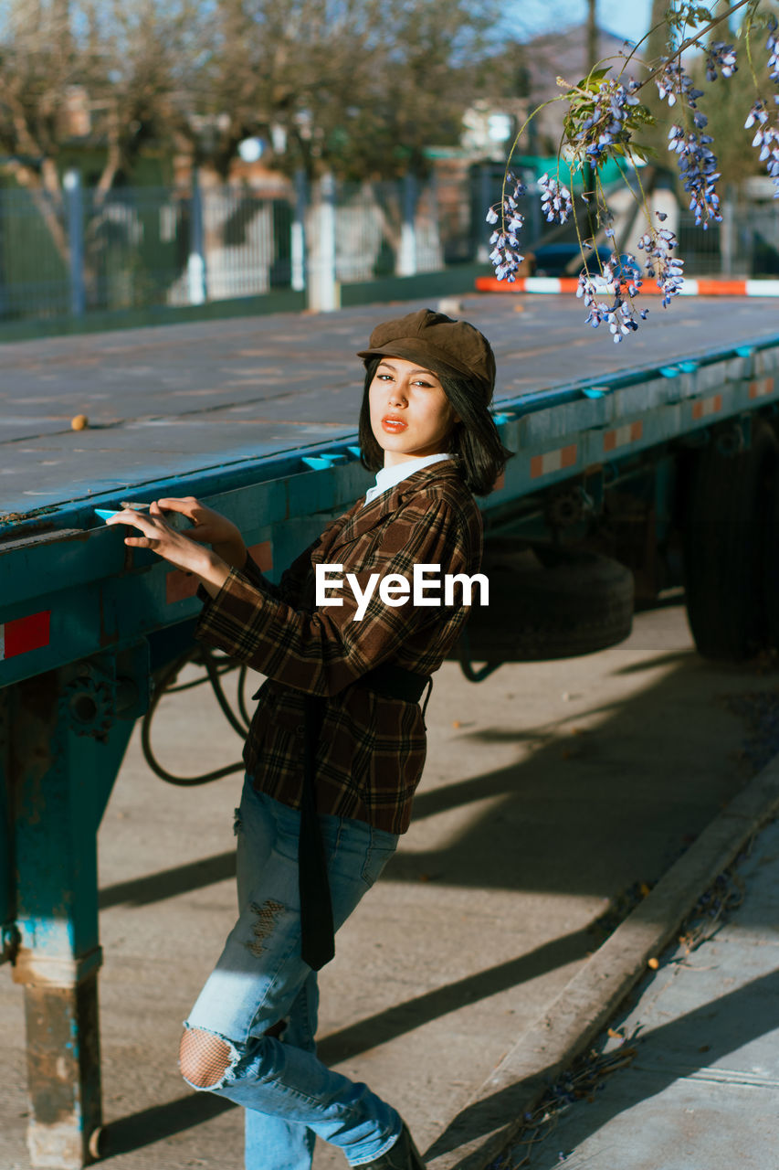 Side view of young stylish ethnic female in beret against aged trailer looking at camera in sunlight