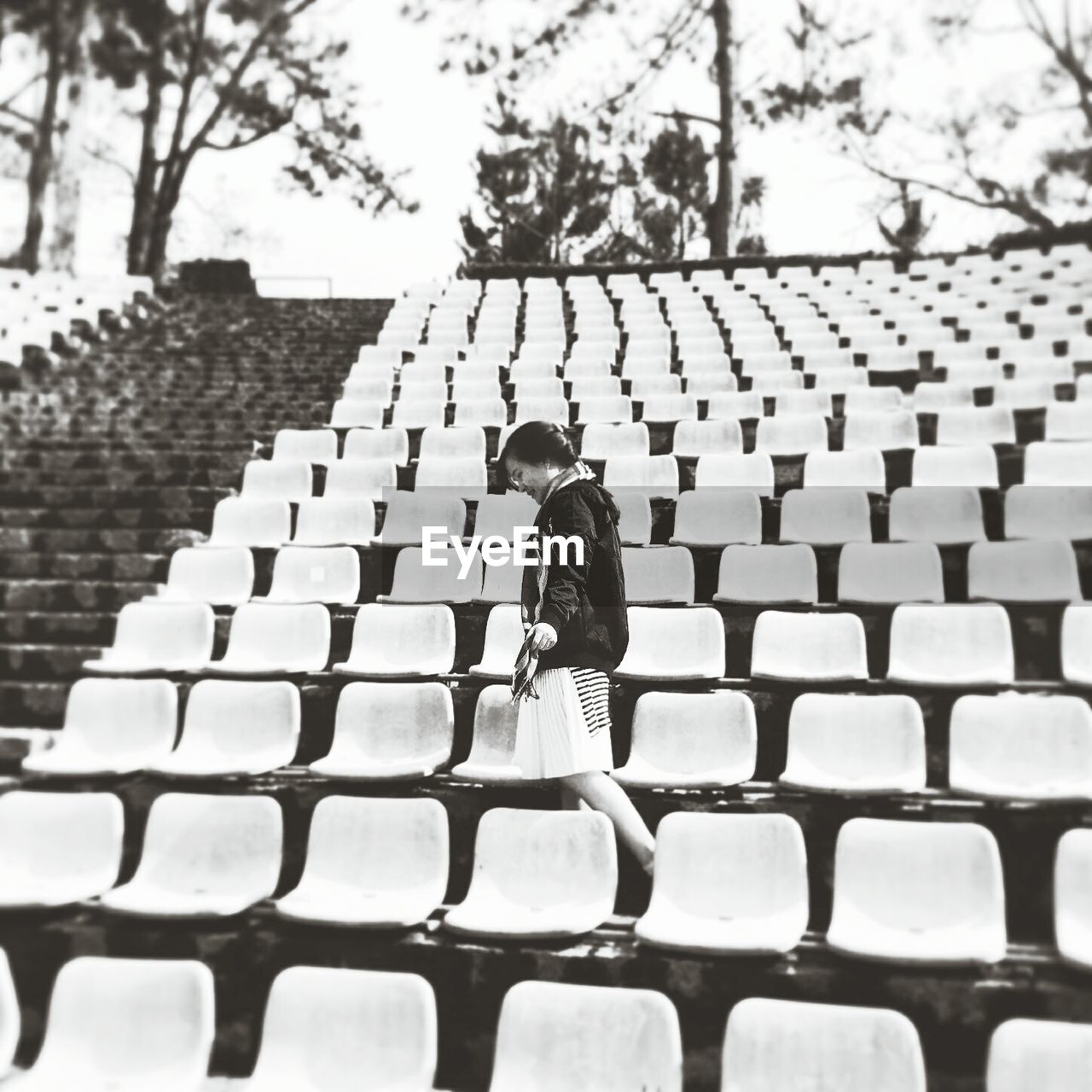 Woman walking amidst chairs against trees