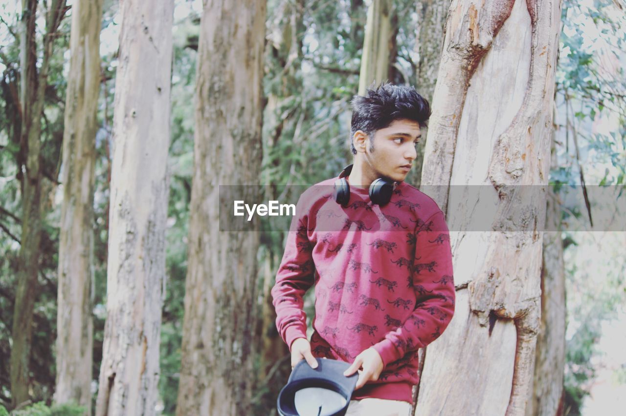 Young man standing by tree trunk