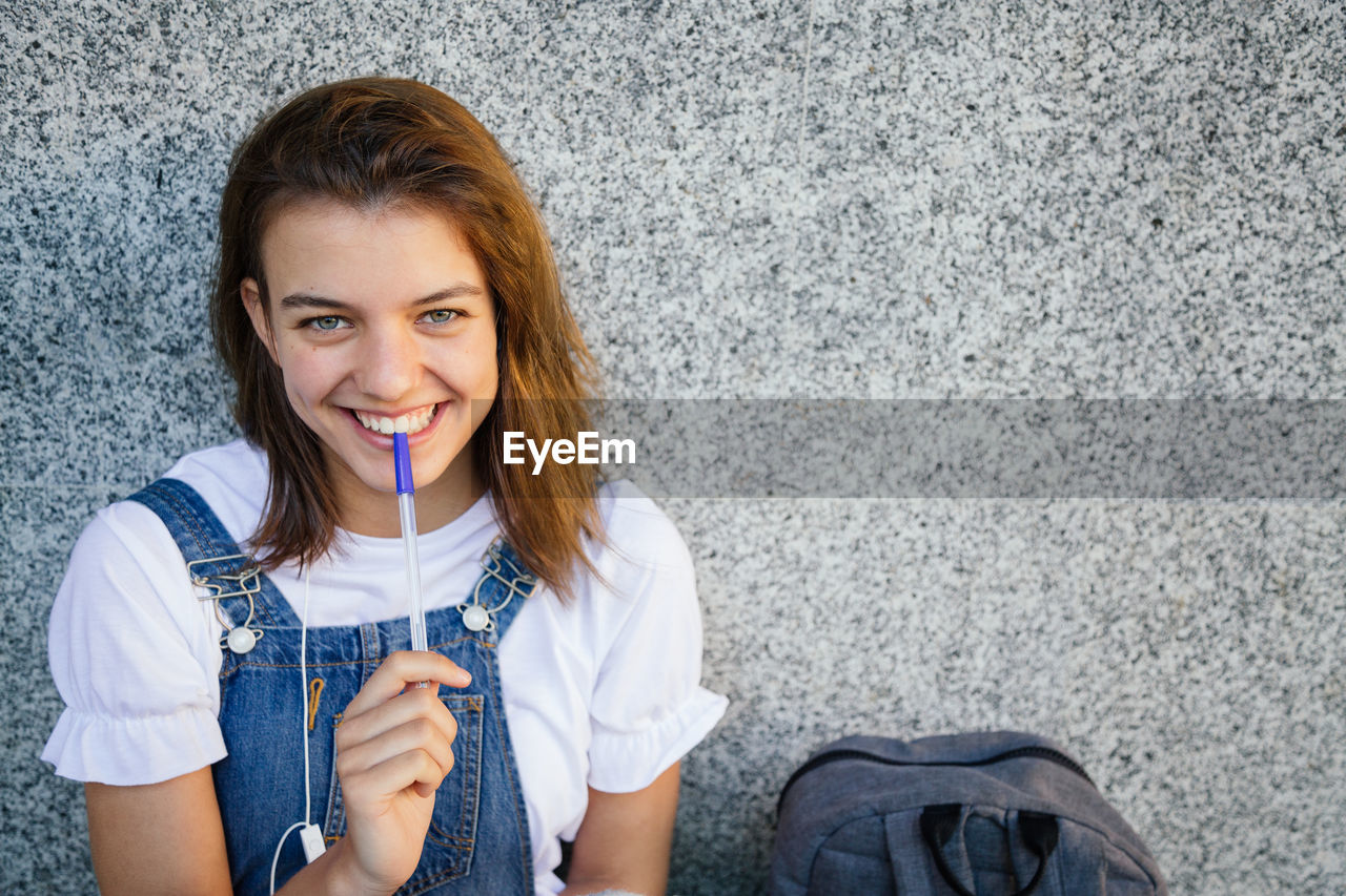 Portrait of smiling teenage girl sitting against wall