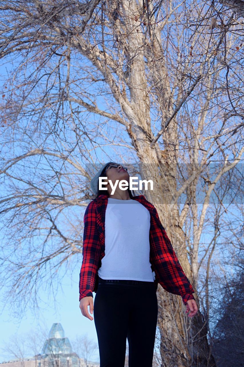 Low angle view of woman standing against bare tree