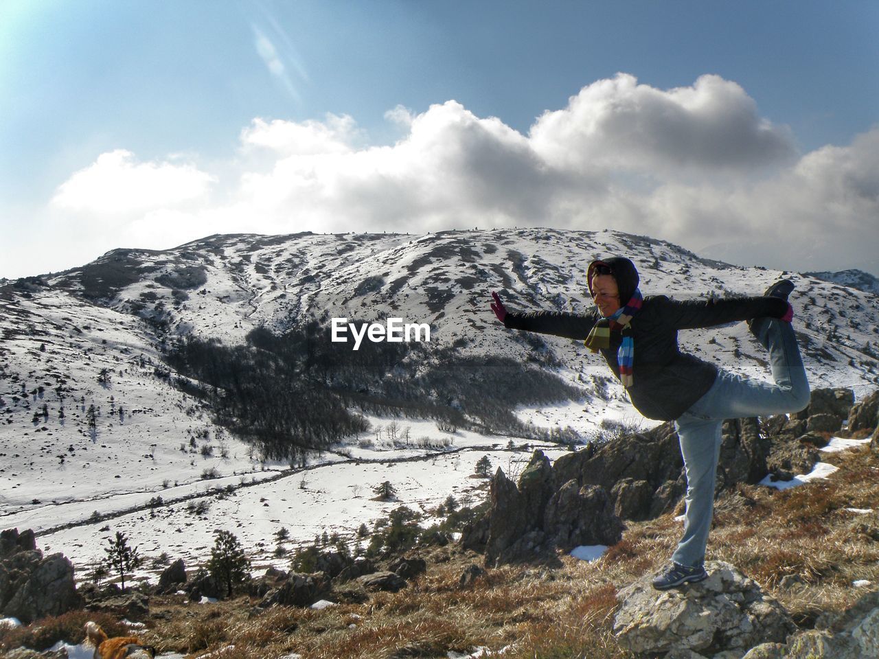 Full length of woman practicing yoga on rock against snowcapped mountain