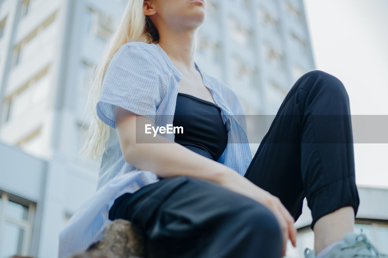 Low angle view of young woman sitting against building