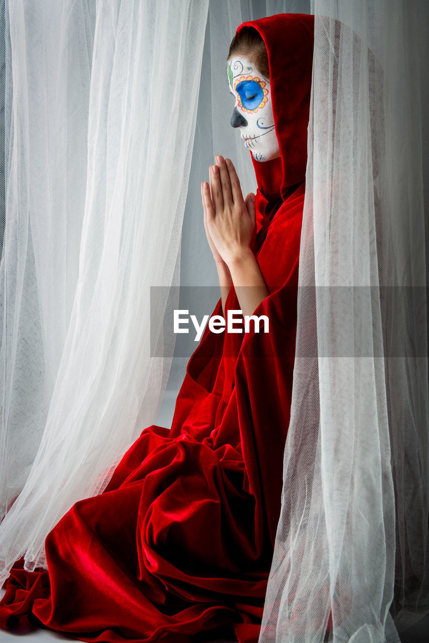 Woman with halloween make-up praying while sitting amidst curtains
