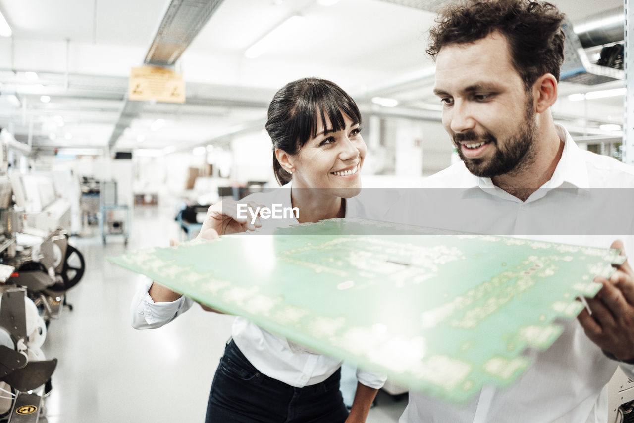 Smiling male and female technicians analyzing large computer chip in industry