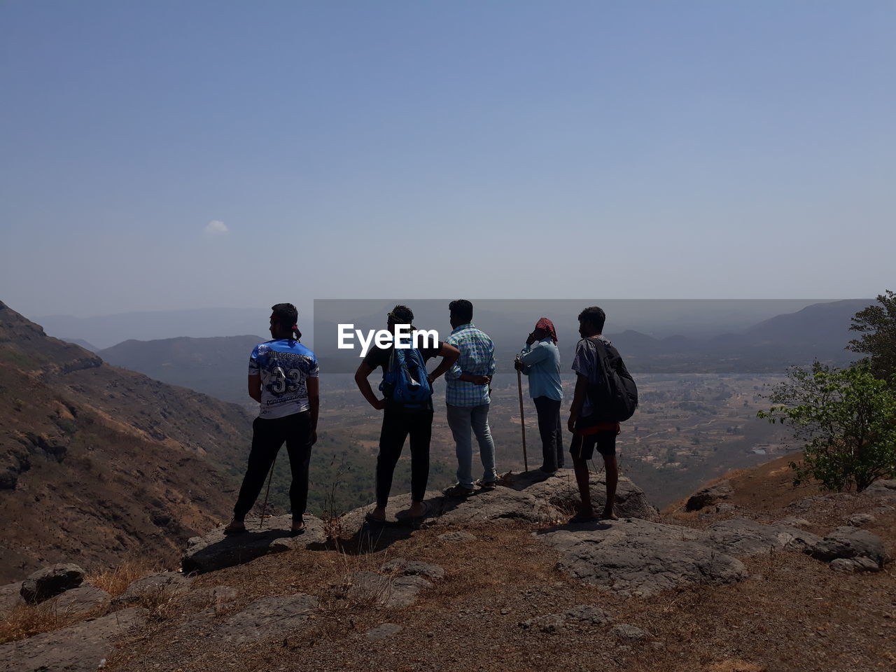 REAR VIEW OF PEOPLE STANDING ON MOUNTAIN