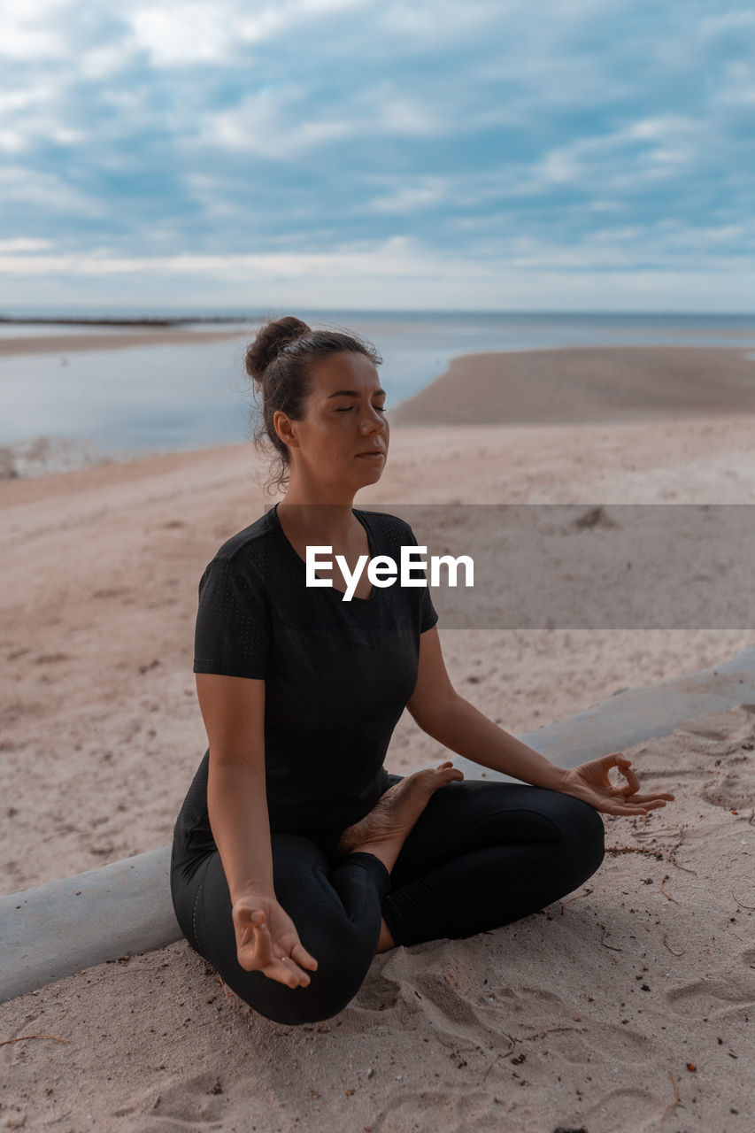 Side view of woman sitting at beach against sky