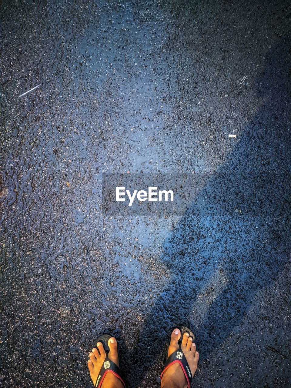 LOW SECTION VIEW OF PERSON STANDING ON WET STREET