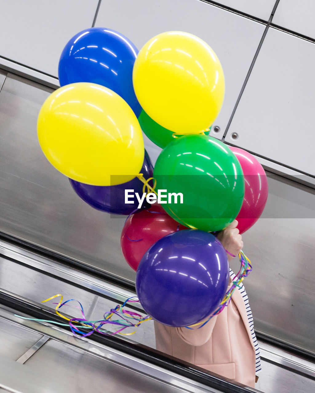 Side view of person holding colorful balloons while standing on escalator