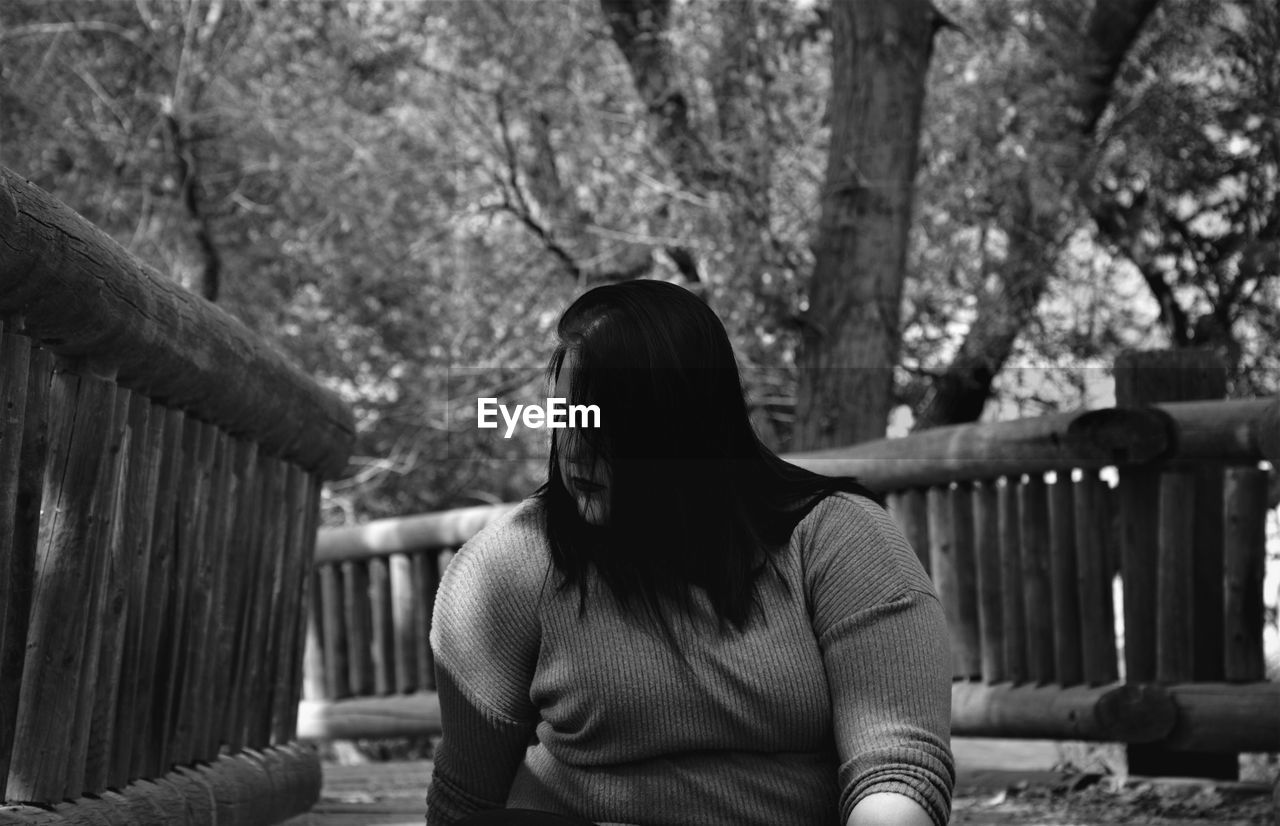 Young woman sitting on footpath against bare trees