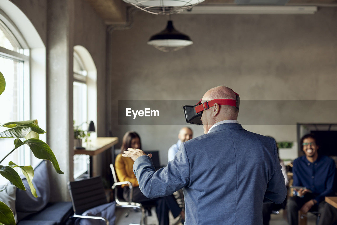 Rear view of mature businessman wearing vr gesturing at creative office