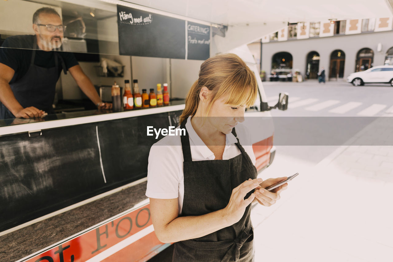 Female chef using mobile phone by food truck at city street