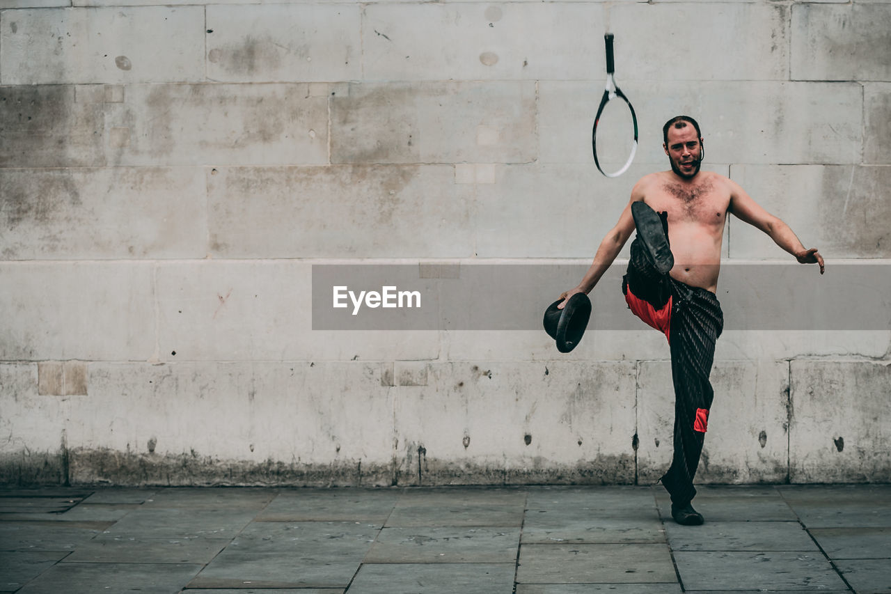 Full length of shirtless man performing while standing against wall