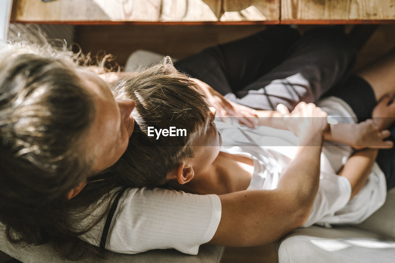 Mother and son lying down on sofa at home during sunny day