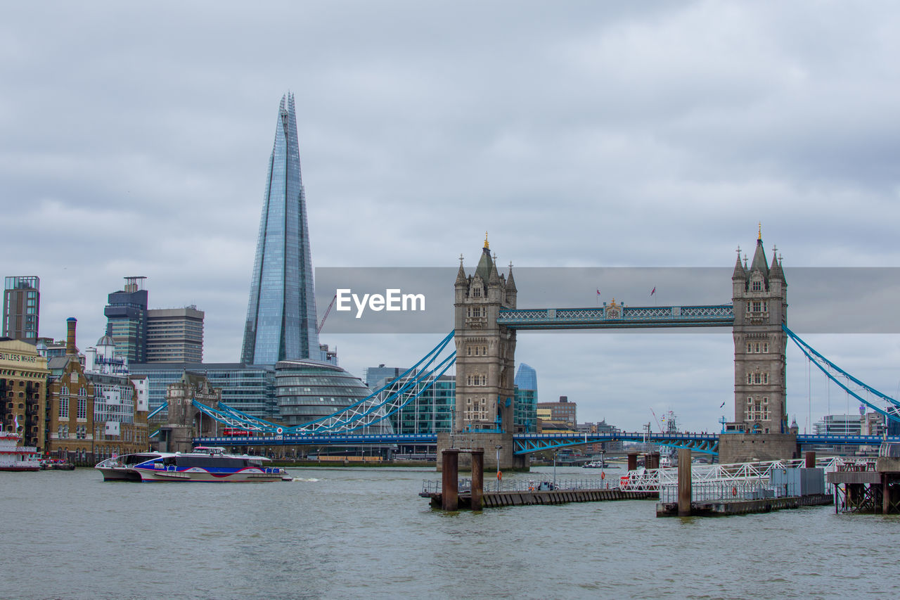 BRIDGE OVER RIVER BY BUILDINGS AGAINST SKY