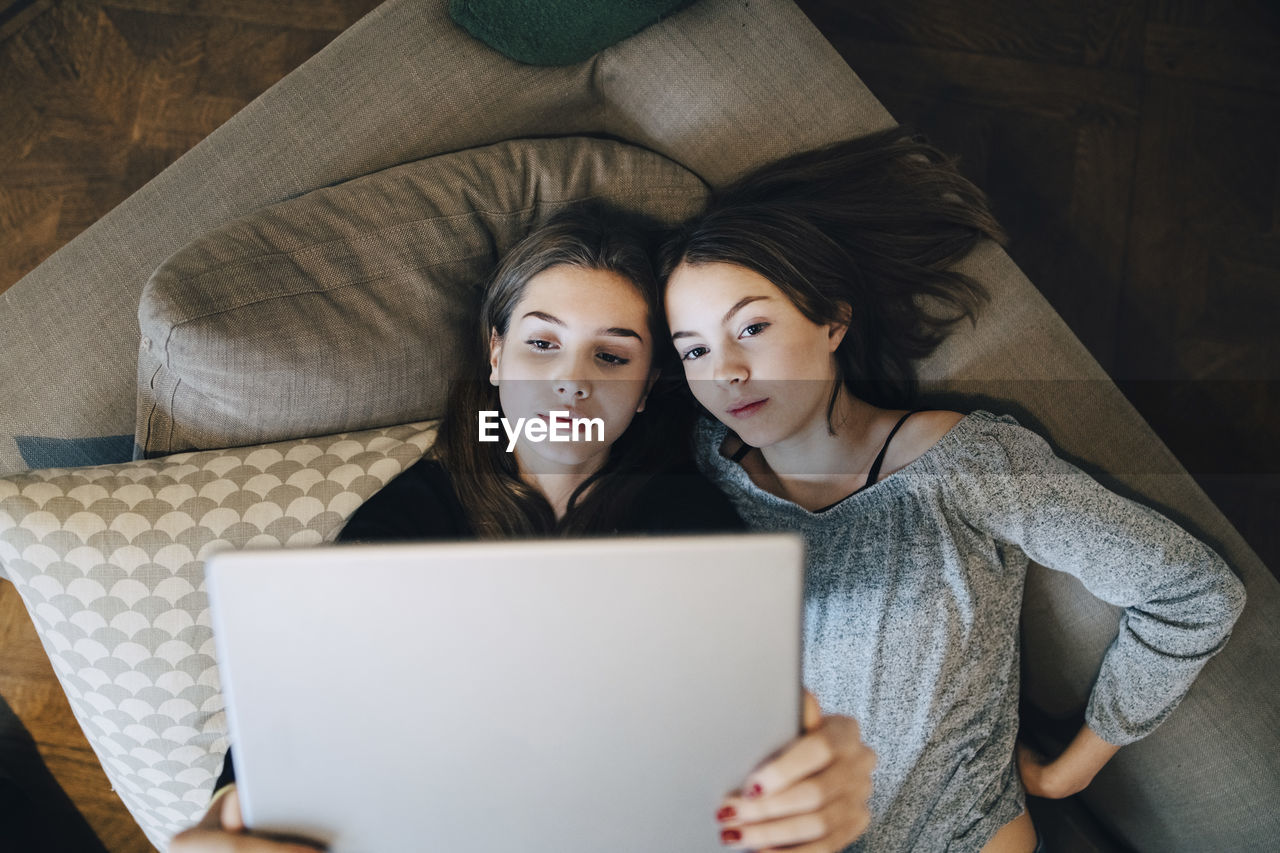 High angle view of girls using laptop while lying on sofa at home