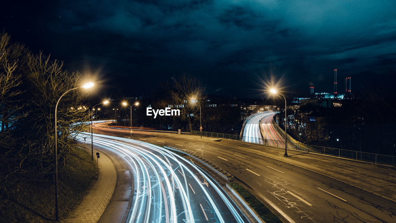 Light trails on road in city against sky at night