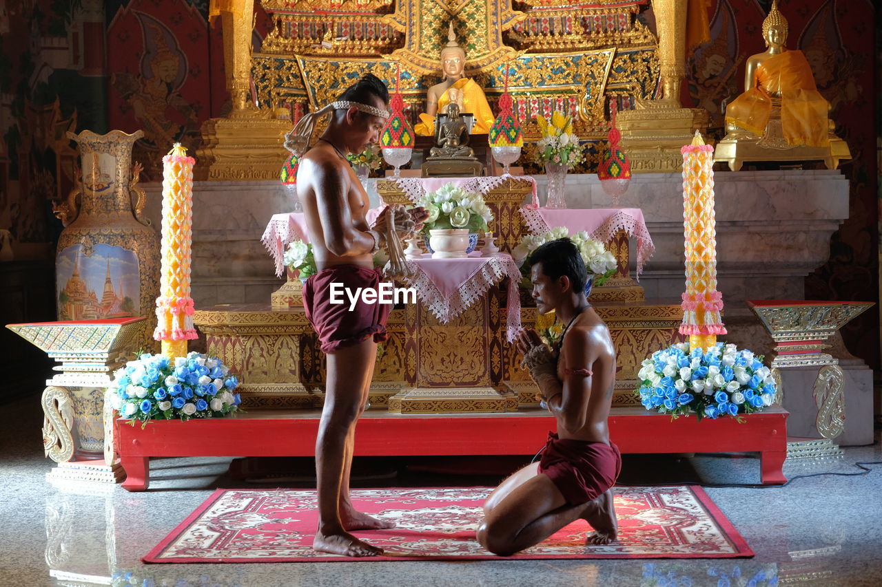 Side view of shirtless men praying in buddhist temple