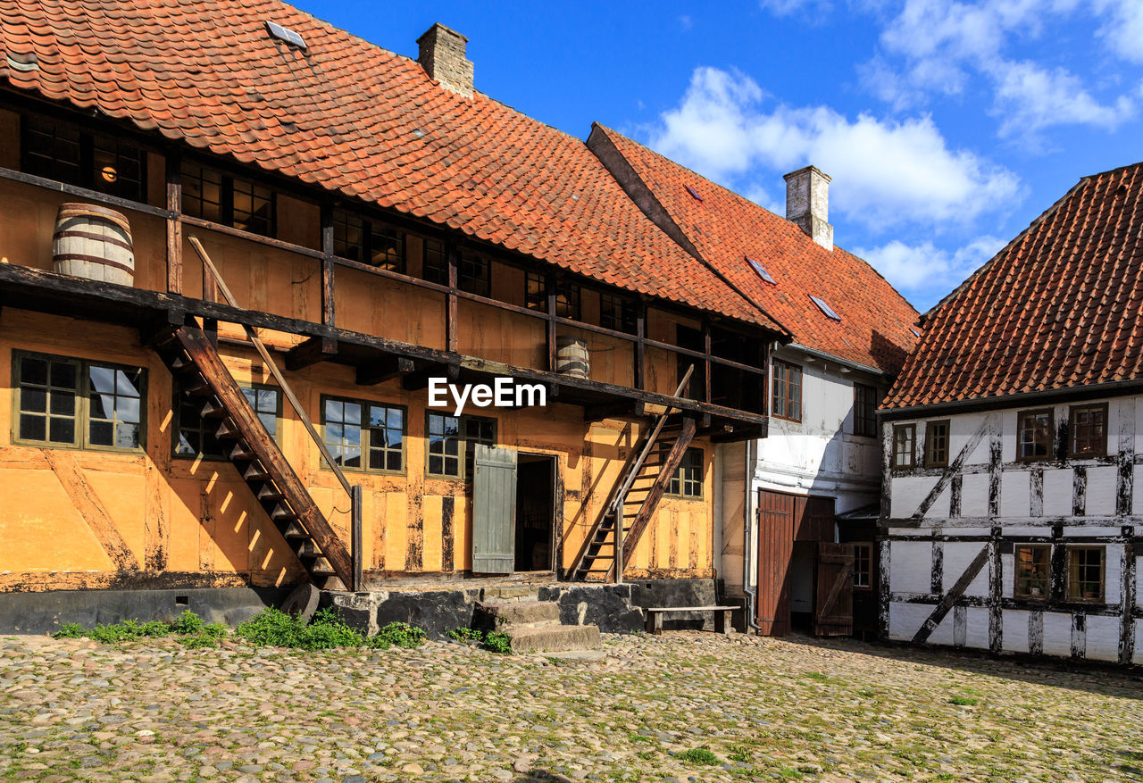 Old houses on field by buildings in city against sky