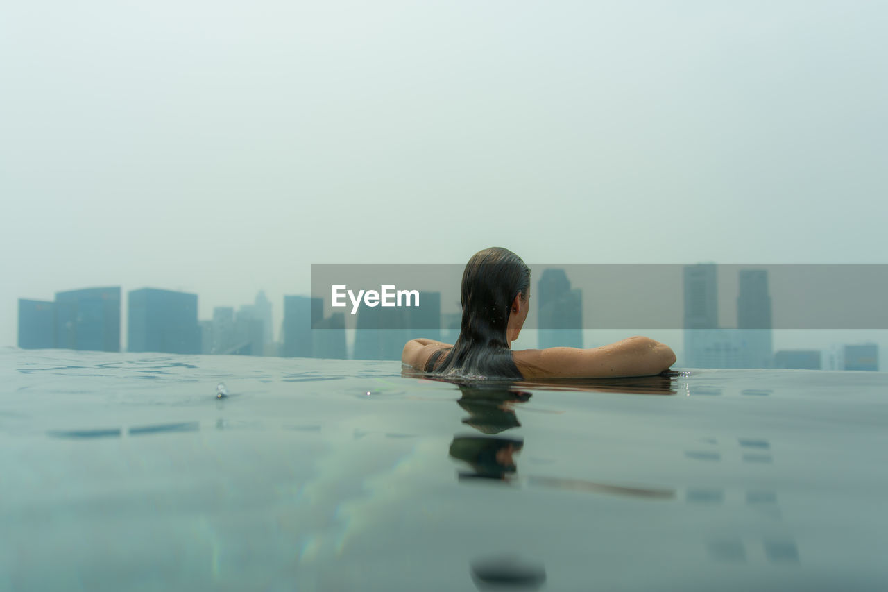 Rear view of woman in infinity pool against skyscrapers