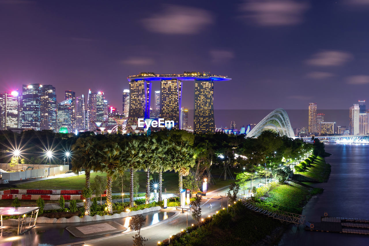 Illuminated buildings by street against sky at night