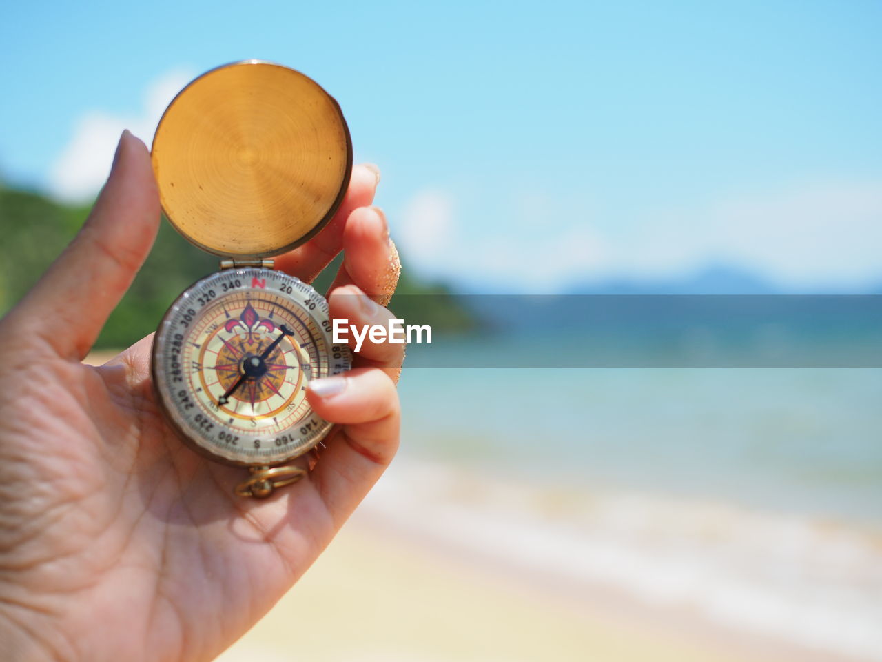 Close-up of hand holding compass at beach against sky
