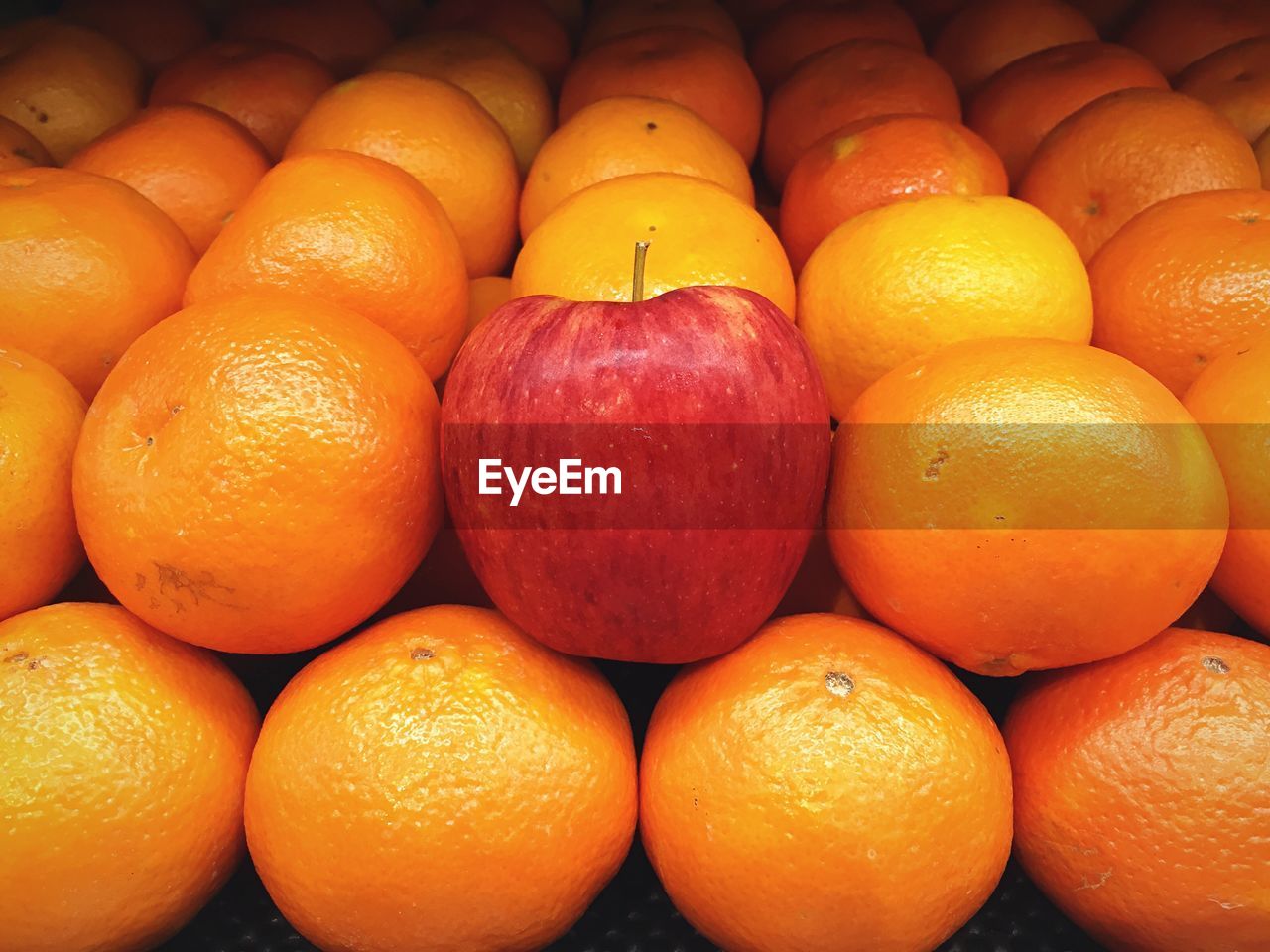 Apple arranged amidst oranges at market stall for sale