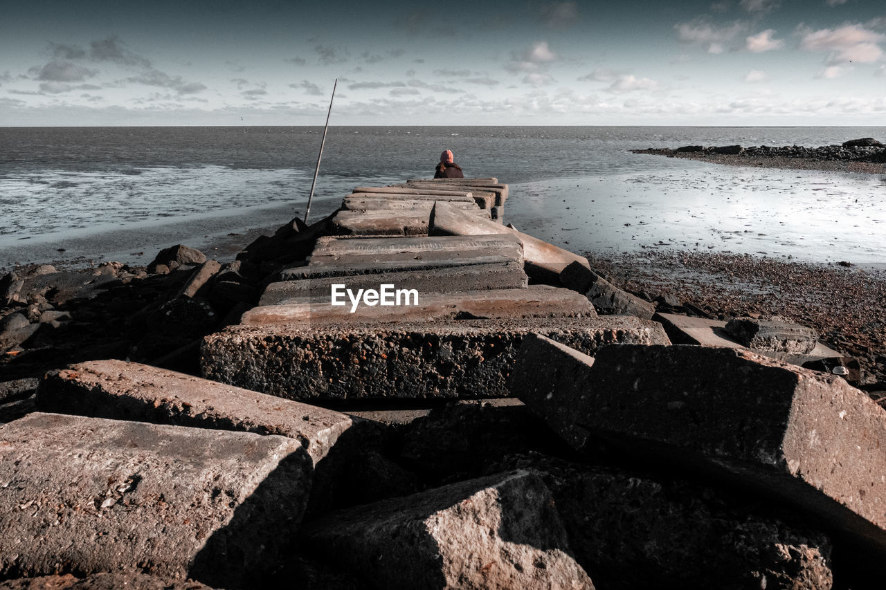 Rear view of woman sitting on rock at beach